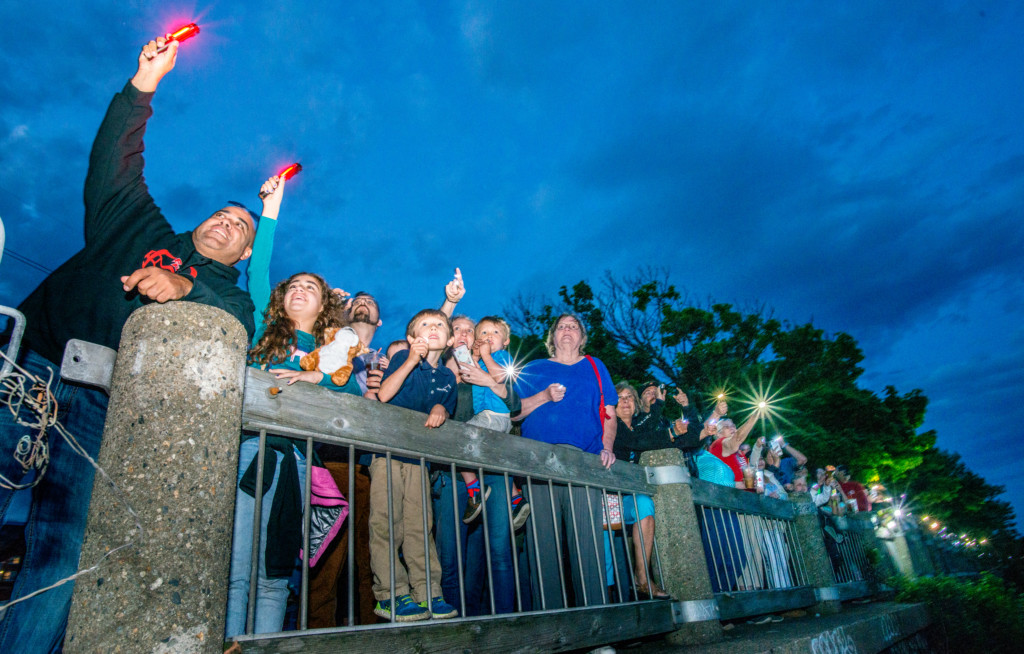 Adults and Children holding up flashlights at night as they participate in the Good Night Lights signal. 