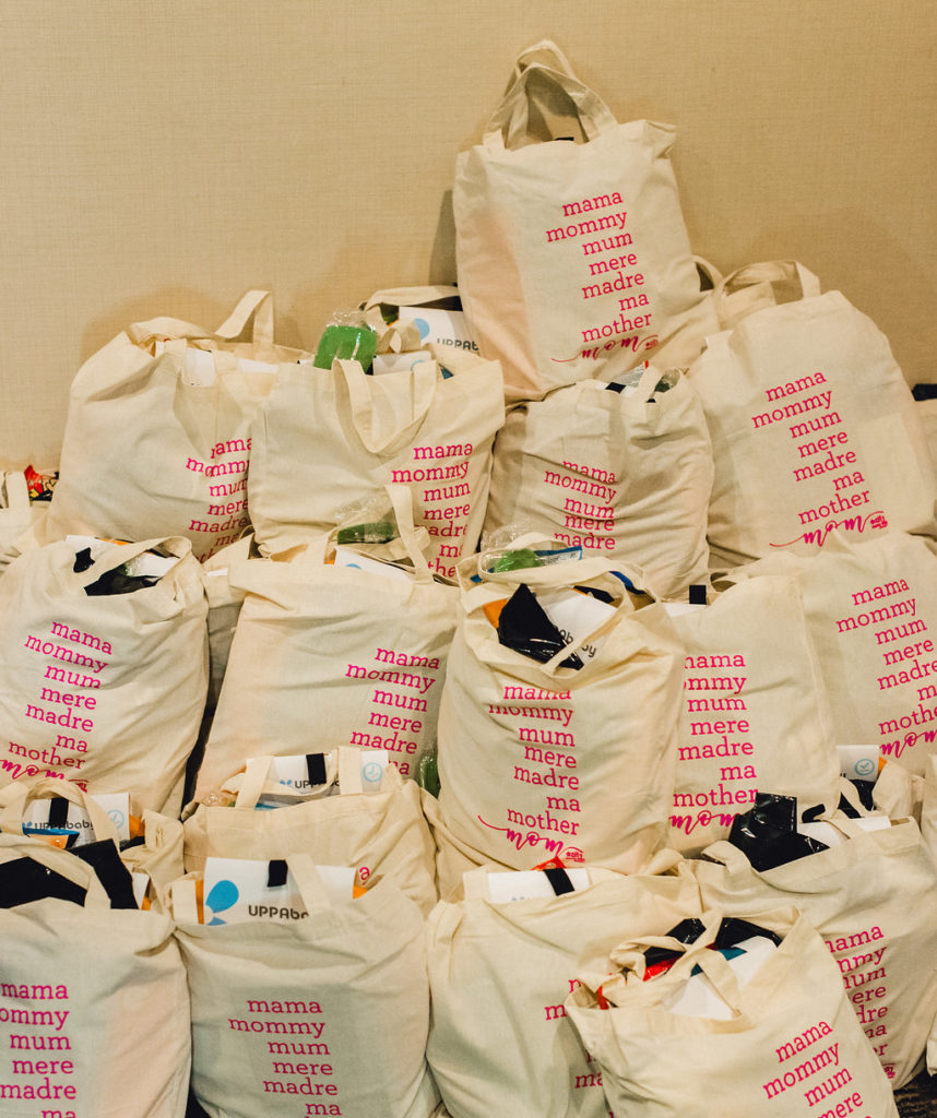Large pile of swag bags with the words "Mama, mommy, mom, mere, madre, ma, mother, mom." in a pile for Providence Moms Blogs New and Expectant Mother Event: Bloom