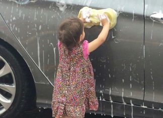 Toddler girl with brown hair in flowered dress washing a car. Providence Moms Blog post on chores.