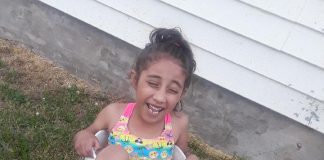 brown child smiling wearing bathing suit in bucket