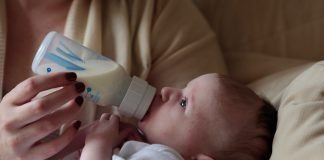 A baby is held in their parent's arms while being fed a bottle of milk