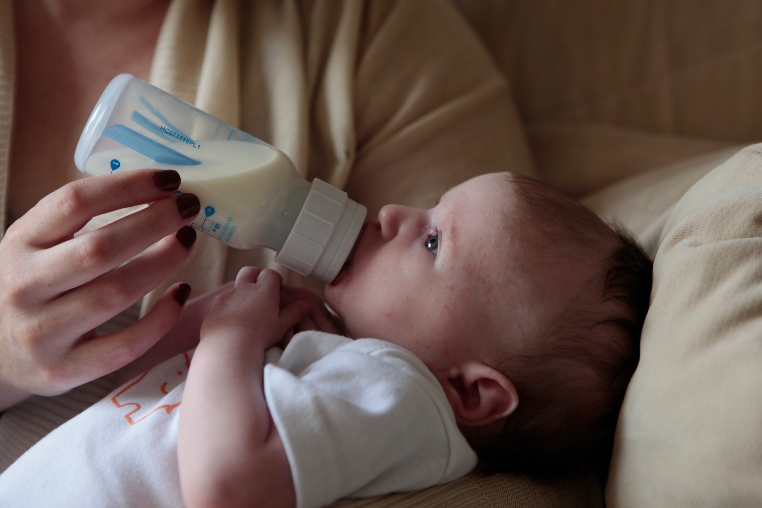 A baby is held in their parent's arms while being fed a bottle of milk 