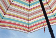 young white boy at the beach under colorful umbrella