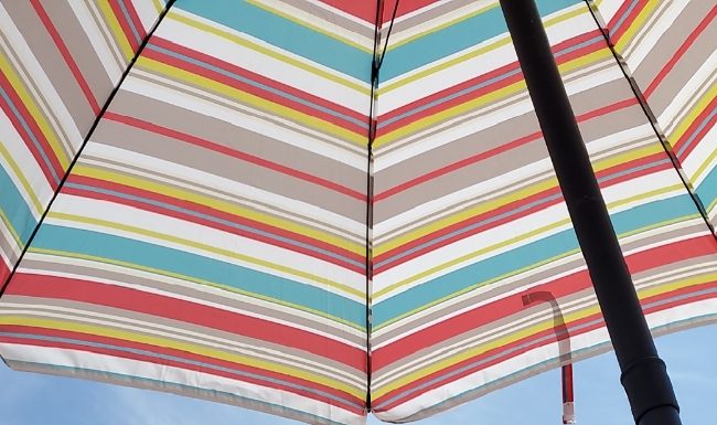 young white boy at the beach under colorful umbrella