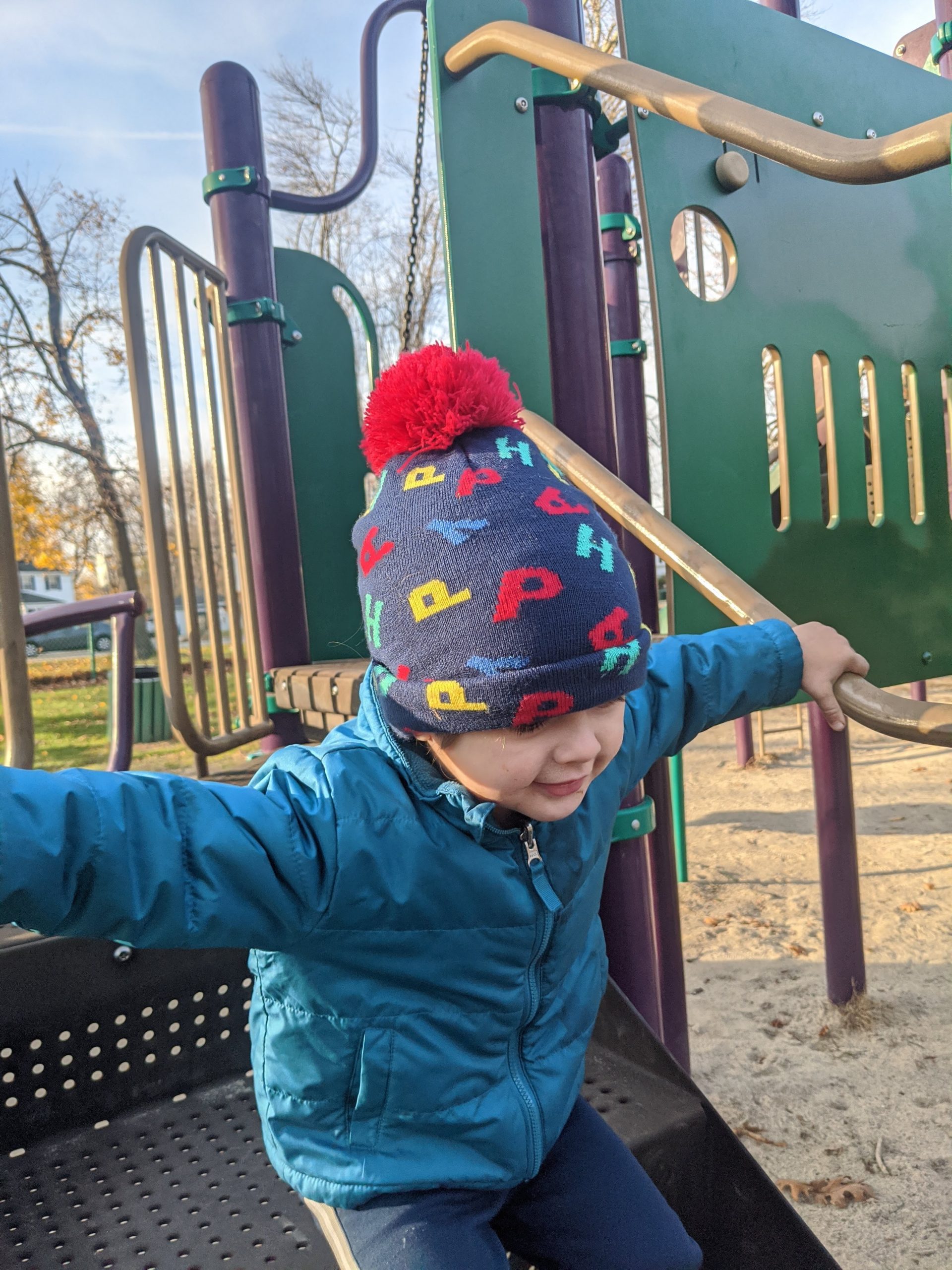 Toddler boy smiles jumping on playground structure 