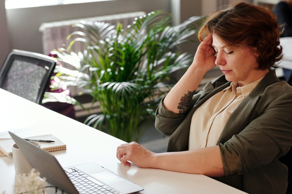 woman with migraine holding her head while working at computer