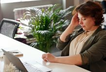 woman with migraine holding her head while working at computer