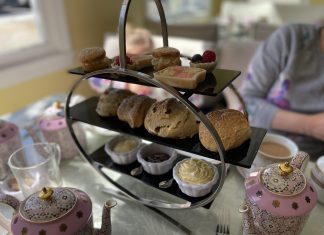 a three tiered stand containing cakes, scones, cream and jam