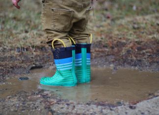 A toddler plays in a mud puddle wearing green rain boots