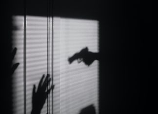 Shadow of a hand pointing a gun at raised hands