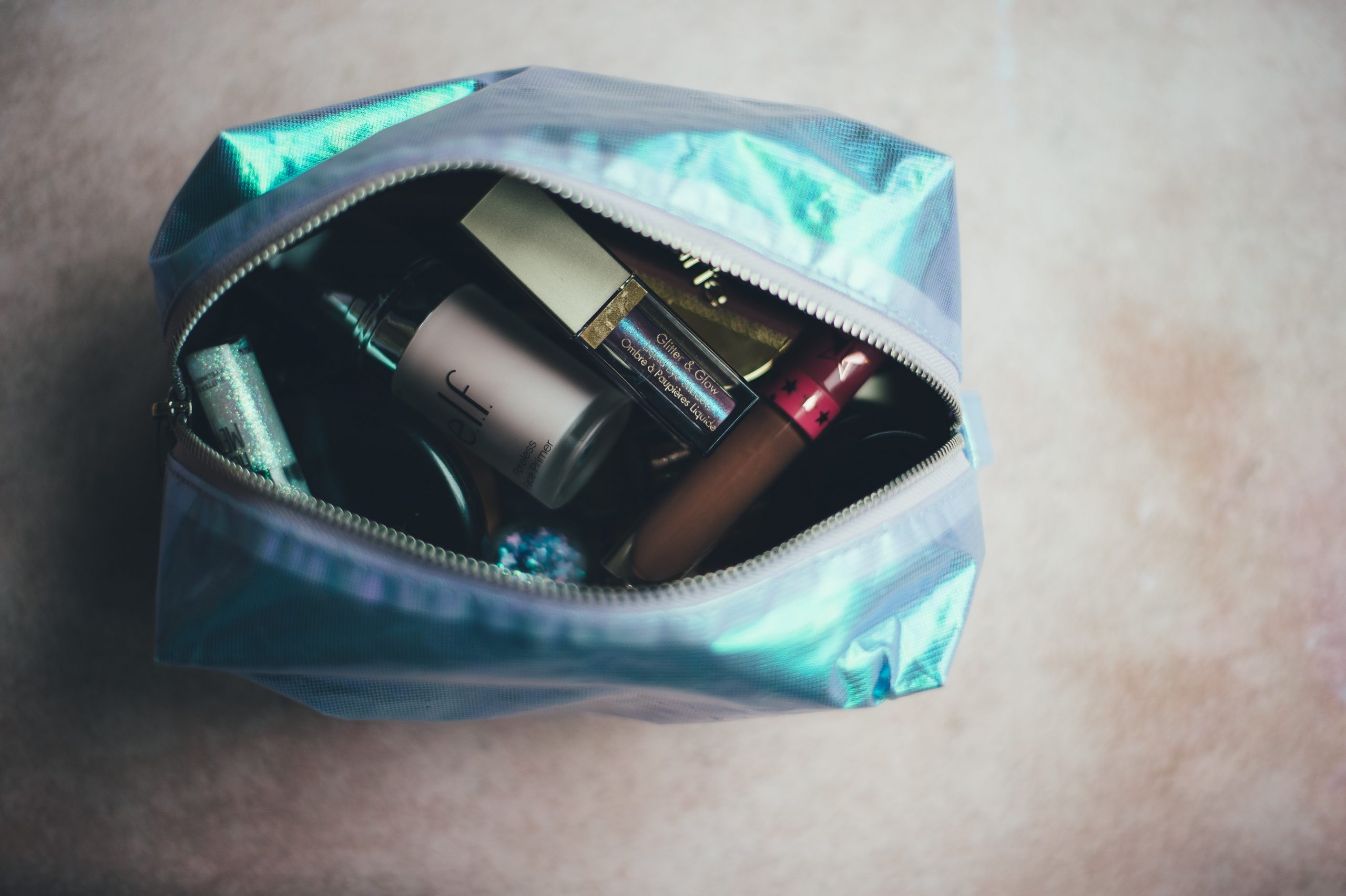 a shiny make up bag with an open zipper showing a jumble of make up inside