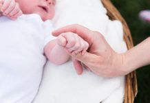 A close up image of a baby's fingers clutching an adults hand against a white background
