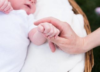 A close up image of a baby's fingers clutching an adults hand against a white background
