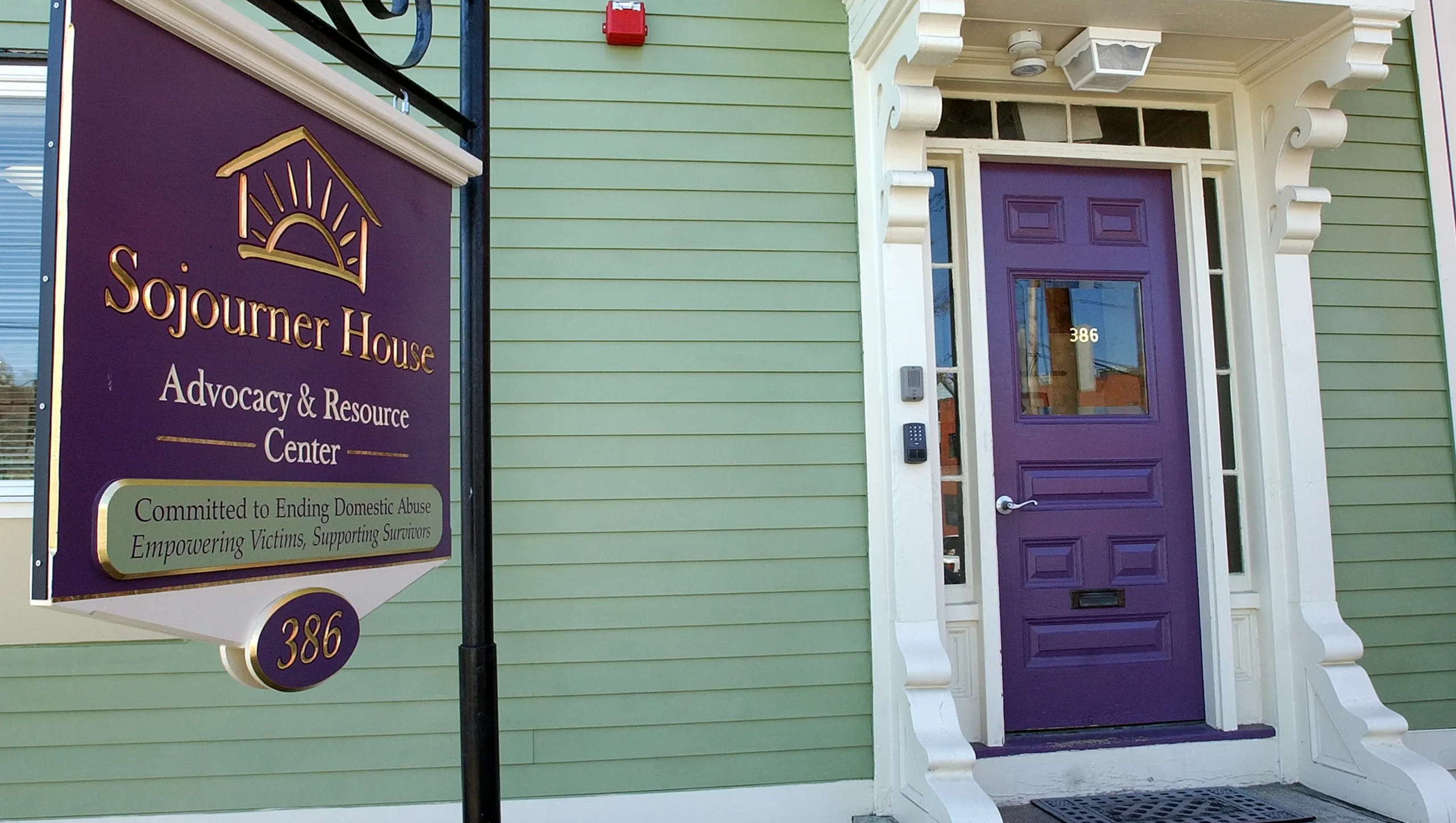 A purple front door is shown with a purple sign next to it which reads 'Sojourner House Advocacy and Resources'